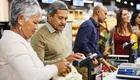 Im Vordergrund ein Paar an der Supermarktkasse, im Hintergrund noch mehrere Personen
