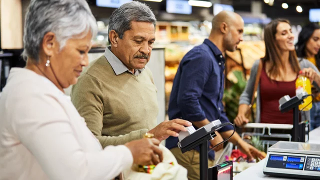 Im Vordergrund ein Paar an der Supermarktkasse, im Hintergrund noch mehrere Personen