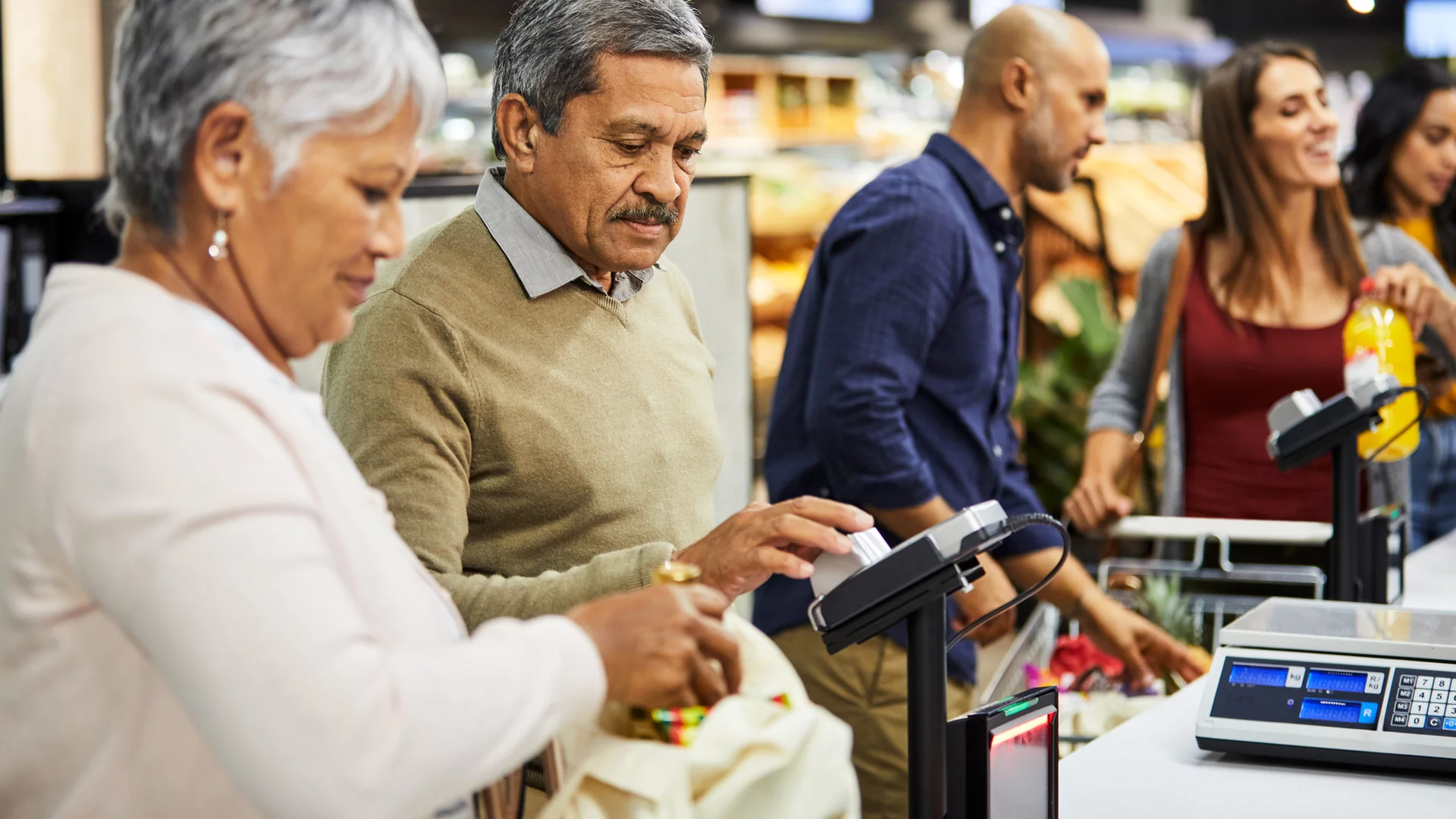 Im Vordergrund ein Paar an der Supermarktkasse, im Hintergrund noch mehrere Personen