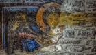 Das Bild zeigt ein Wandgemälde eines Engels mit Flügeln und einem Heiligenschein. Der Engel ist frontal abgebildet und scheint nach vorne zu schauen. Die Farben sind überwiegend Blau, Gold und Beige, wobei die Mauer im Hintergrund aus unregelmäßigen Steinen besteht.