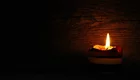 Eine brennende Kerze auf einem dunklen Hintergrund, die warmes Licht spendet. Die Kerze hat mehrere Schichten in verschiedenen Farben. Die Flamme flackert sanft.