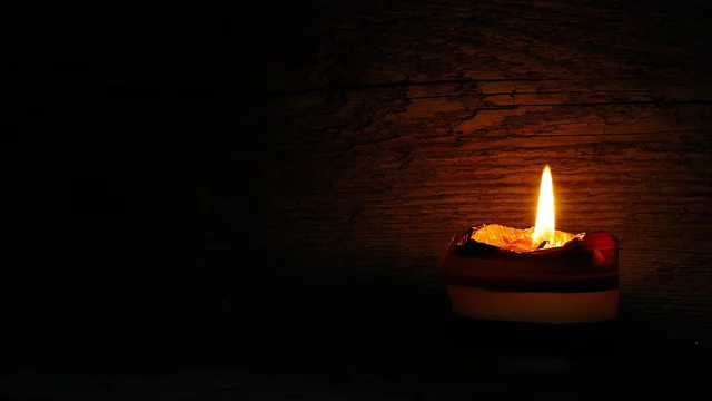 Eine brennende Kerze auf einem dunklen Hintergrund, die warmes Licht spendet. Die Kerze hat mehrere Schichten in verschiedenen Farben. Die Flamme flackert sanft.