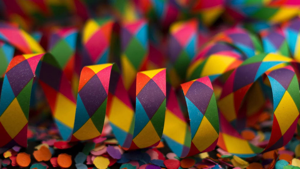 Bunte Papierteile in Form von geschwungenen Streifen und Konfetti in verschiedenen Farben. Die Streifen sind im Rautenmuster gestaltet und in lebhaften Farben gehalten, was eine festliche Atmosphäre vermittelt. Diese Anordnung scheint für eine Feier oder einen festlichen Anlass gedacht zu sein.