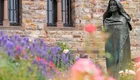 Hildegard von Bingen als Bronze-Statur "stehend" vor einer Kirche