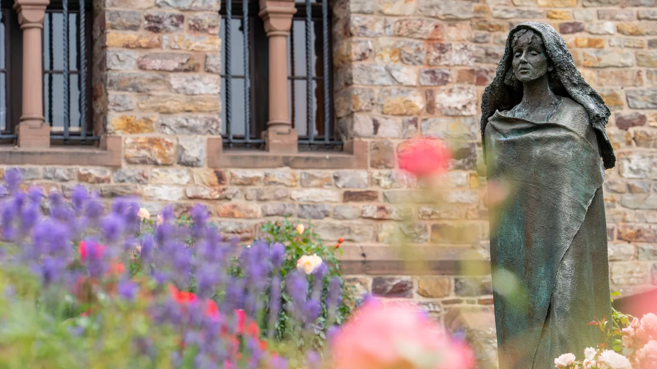 Hildegard von Bingen als Bronze-Statur "stehend" vor einer Kirche