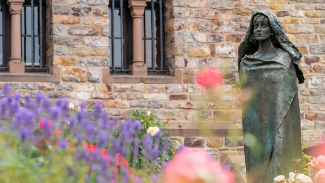 Hildegard von Bingen als Bronze-Statur "stehend" vor einer Kirche