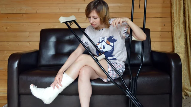 Eine Frau sitzt auf einem Sofa mit bandagiertem Bein. 