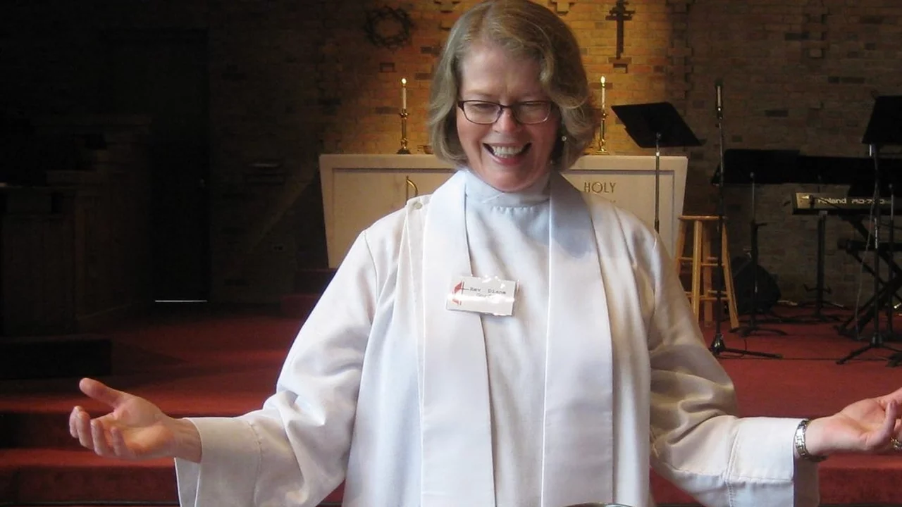 Eine lächelnde Frau in einem weißen Gewand steht mit ausgebreiteten Armen vor einem Altar in einer Kirche. Sie strahlt Freude und Offenheit aus, während sie eine geistliche Botschaft übermittelt. Der Hintergrund zeigt eine entspannte, kirchliche Umgebung mit Holz- und Lichtelementen.