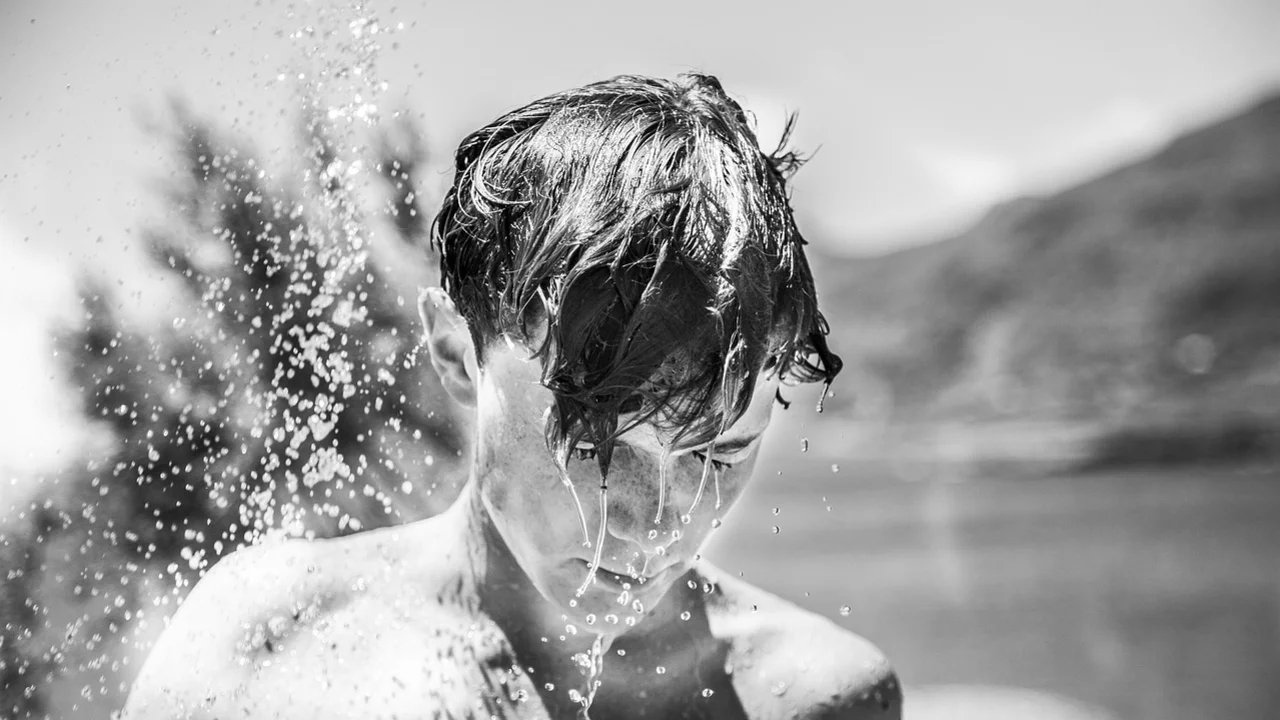 Junge steht unter einer warmen Dusche.