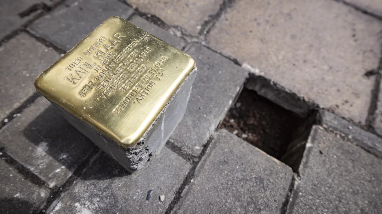 Ein Stolperstein aus Bronze mit der Inschrift zu Ehren von Karl W. Heimer. Er gehört zu einer Gedenkaktion für Opfer des Nationalsozialismus. Der Stein liegt auf dem Gehweg, umgeben von Pflastersteinen und einem leeren Platz, wo ein weiterer Stein platziert werden könnte.