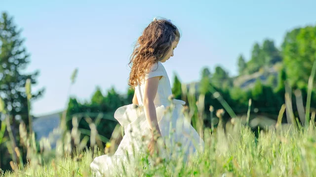 Ein Mädchen geht über eine sommerliche Wiese spazieren. 