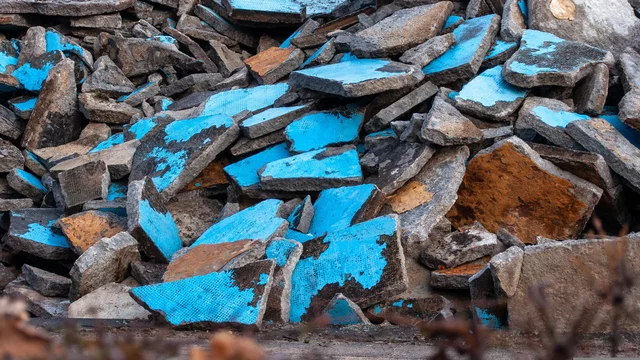 Ein Haufen von abgebrochenen Betonplatten in verschiedenen Farben, vor allem in Blau und Grau. Die Platten sind unordentlich übereinander gestapelt und zeigen verschiedene Oberflächenstrukturen, die durch Abnutzung und Witterung geprägt sind.