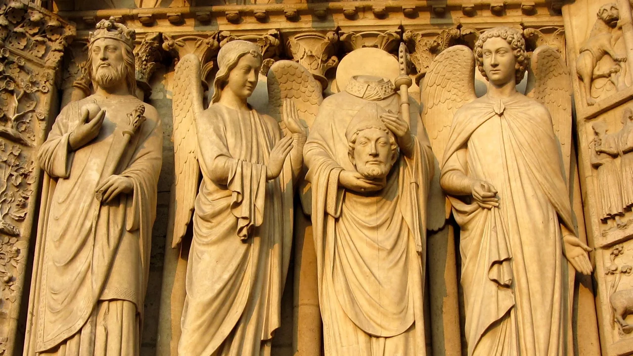 Reliefs an einer Kathedrale zeigen vier Figuren: links ein König, daneben ein Engel, der die Hände hebt. In der Mitte steht eine Figur mit einem Kopf in der Hand, rechts ein weiterer Engel. Die Figuren sind detailliert gestaltet und symbolisieren biblische Themen.