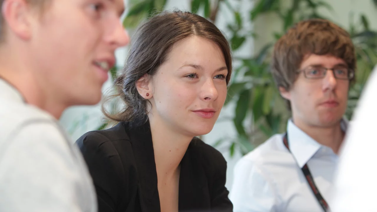 Drei Personen hören aufmerksam einem Redner zu. 