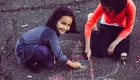 Zwei Kinder sitzen auf dem Asphalt und zeichnen mit Kreide. Ein Mädchen lächelt fröhlich, während sie an einer bunten Zeichnung arbeitet. Das andere Kind konzentriert sich ebenfalls auf das Malen. Die Szene vermittelt Freude und Kreativität beim Spielen im Freien.
