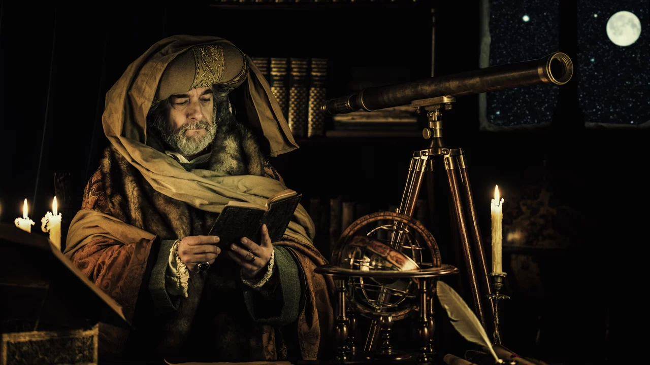 Ein weiser Mann mit einem langen Bart trägt einen prachtvollen Umhang und hält ein Buch in der Hand. Er steht an einem Tisch, neben einem Teleskop und einer astronomischen Armillarsphäre. Im Hintergrund sind Sterne und der Mond sichtbar. Kerzen sorgen für schwaches Licht.