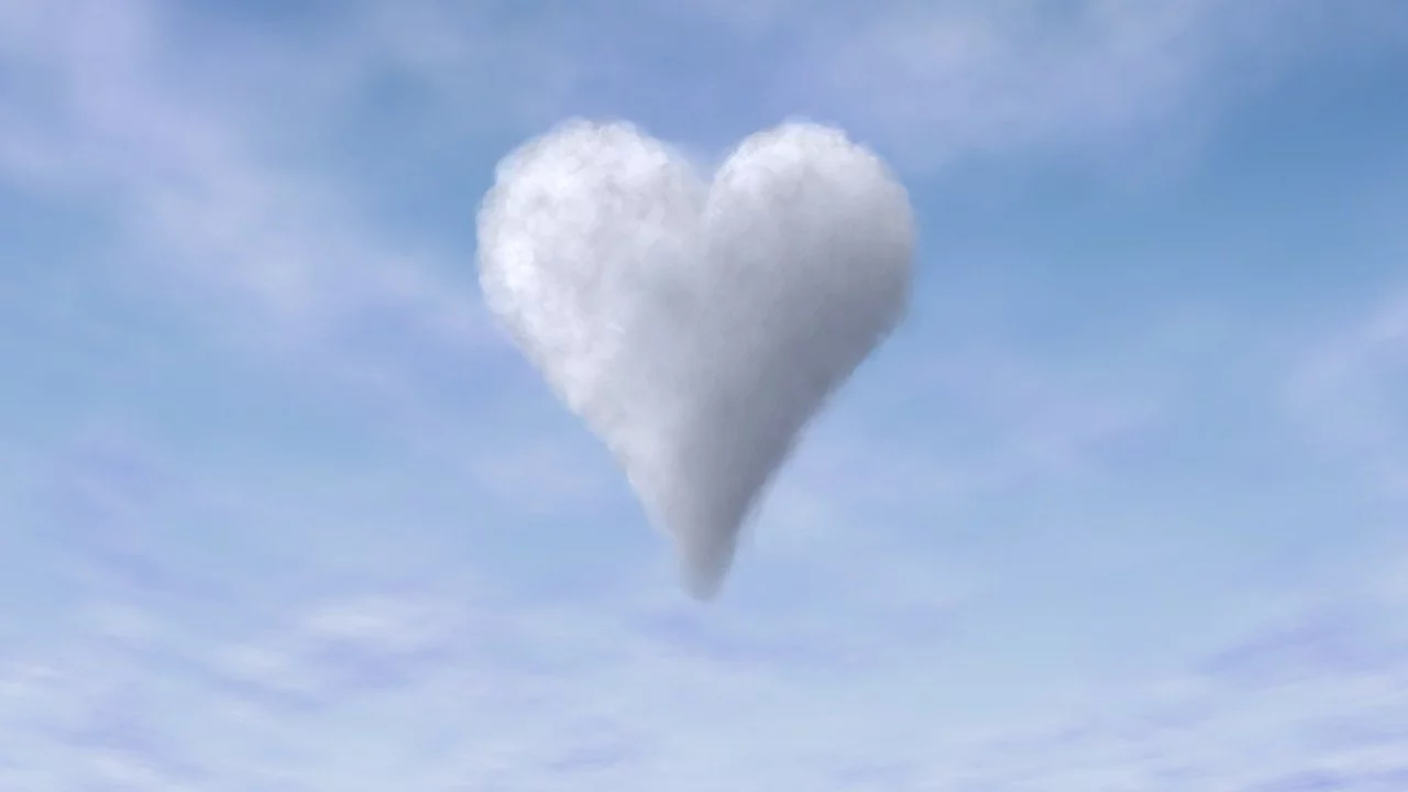 Eine herzförmige Wolke schwebt vor einem blauen Himmel. Die Wolke ist weich und flauschig, umgeben von leichter Bewölkung, die die romantische und verspielte Stimmung unterstreicht.