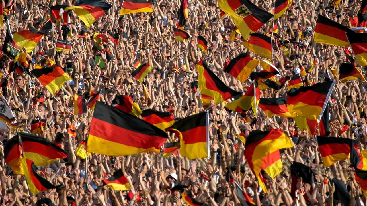 Eine große Menschenmenge feiert begeistert und schwenkt zahlreiche deutsche Flaggen. Die Atmosphäre ist voller Energie und Zusammengehörigkeit, wobei die Fahnen in verschiedenen Höhen und Richtungen gehoben werden.