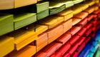 Ein Regal mit farbigem Papier in verschiedenen Tönen. Die Farben verlaufen von grün über gelb, orange und rot bis hin zu blau. Die Papiere sind ordentlich gestapelt und zeigen eine harmonische Farbverlauf.