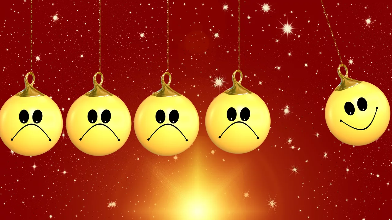 Fünf hängende, goldene Weihnachtskugeln sind zu sehen. Vier Kugeln haben traurige Gesichter, während eine Kugel ein glückliches Gesicht zeigt. Der Hintergrund ist rot mit funkelnden Punkten, die eine festliche Atmosphäre schaffen.