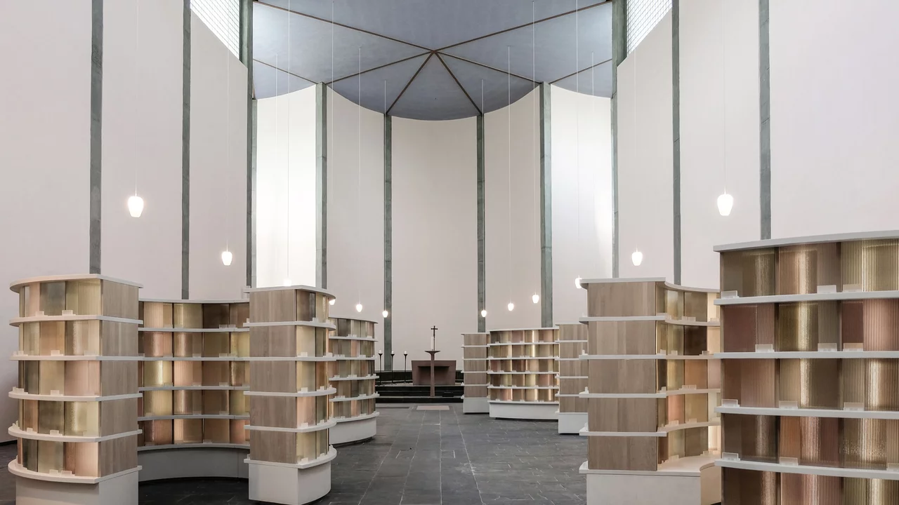 Die Darstellung zeigt einen modernen Raum mit mehreren Buchregalen, die in geschwungener Anordnung angeordnet sind. Der Boden ist aus dunklem Stein, und die Wände sind hoch und hell. In der Mitte steht ein Tisch, und es gibt eine sanfte Beleuchtung von hängenden Lampen.