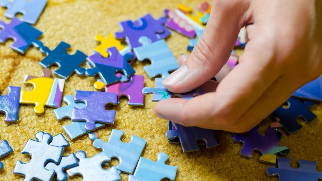 Man sieht eine Hand, die auf einem gelben Untergrund Puzzleteile sortiert.