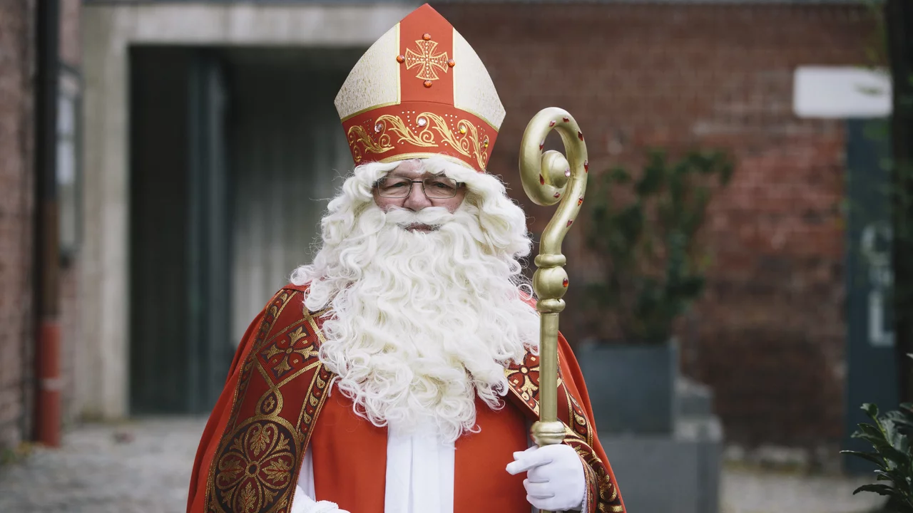 Der Nikolaus in traditioneller Bischofskleidung. Er trägt einen roten Mantel mit goldenen Verzierungen, eine große Bischofsmütze und hat einen langen weißen Bart. In der Hand hält er einen goldenen Bischofsstab. 