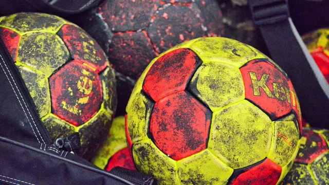 Im Bild sind mehrere Handbälle in verschiedenen Farben zu sehen. Hauptsächlich grün und gelb mit roten Akzenten, teilweise abgenutzt und schmutzig. Die Bälle liegen in einer schwarzen Tasche und sind unterschiedlich angeordnet.