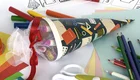 Das Bild zeigt eine traditionelle Schultüte in Form einer gefüllten, bunten Papiertüte. Um die Tüte herum sind Bastelmaterialien wie Buntstifte, Papier und eine Locher zu sehen. Die Schultüte symbolisiert den Beginn des neuen Schuljahres für Kinder.