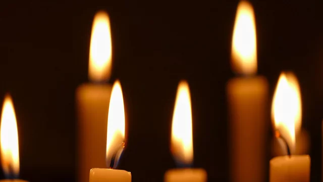 Mehrere Kerzen mit flammendem Docht stehen im Dunkeln. Die sanften, warmen Lichter erzeugen eine beruhigende Atmosphäre. Einige Kerzen sind näher zur Kamera, andere weiter entfernt.