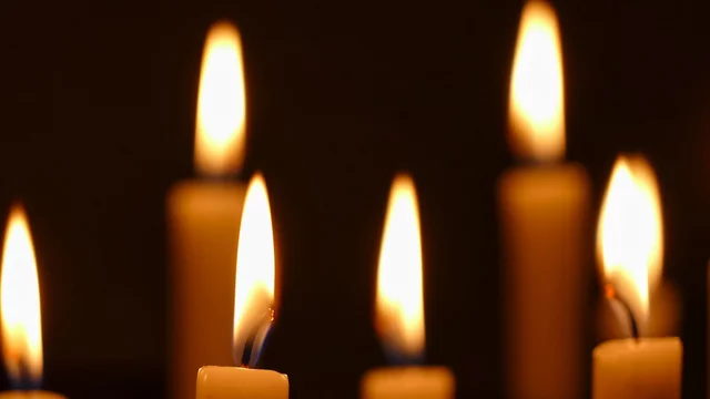 Mehrere Kerzen mit flackernden Flammen stehen auf einer dunklen Oberfläche. Die Lichtstrahlen der Flammen verleihen der Szene eine ruhige, gefühlvolle Atmosphäre. Die Kerzen sind in unterschiedlichen Höhen angeordnet und leuchten sanft im Dunkeln.