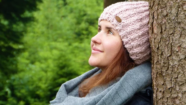 Eine Frau lehnt an einem Baum und schaut nachdenklich in den Himmel.