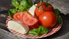 Eine flache, karierte Platte mit frischen, roten Tomaten, halbierten Tomaten, Mozzarella und frischem Basilikum. Die Zutaten sind farbenfrohe und appetitliche Lebensmittel, die für einen Salat oder eine Vorspeise geeignet sind.
