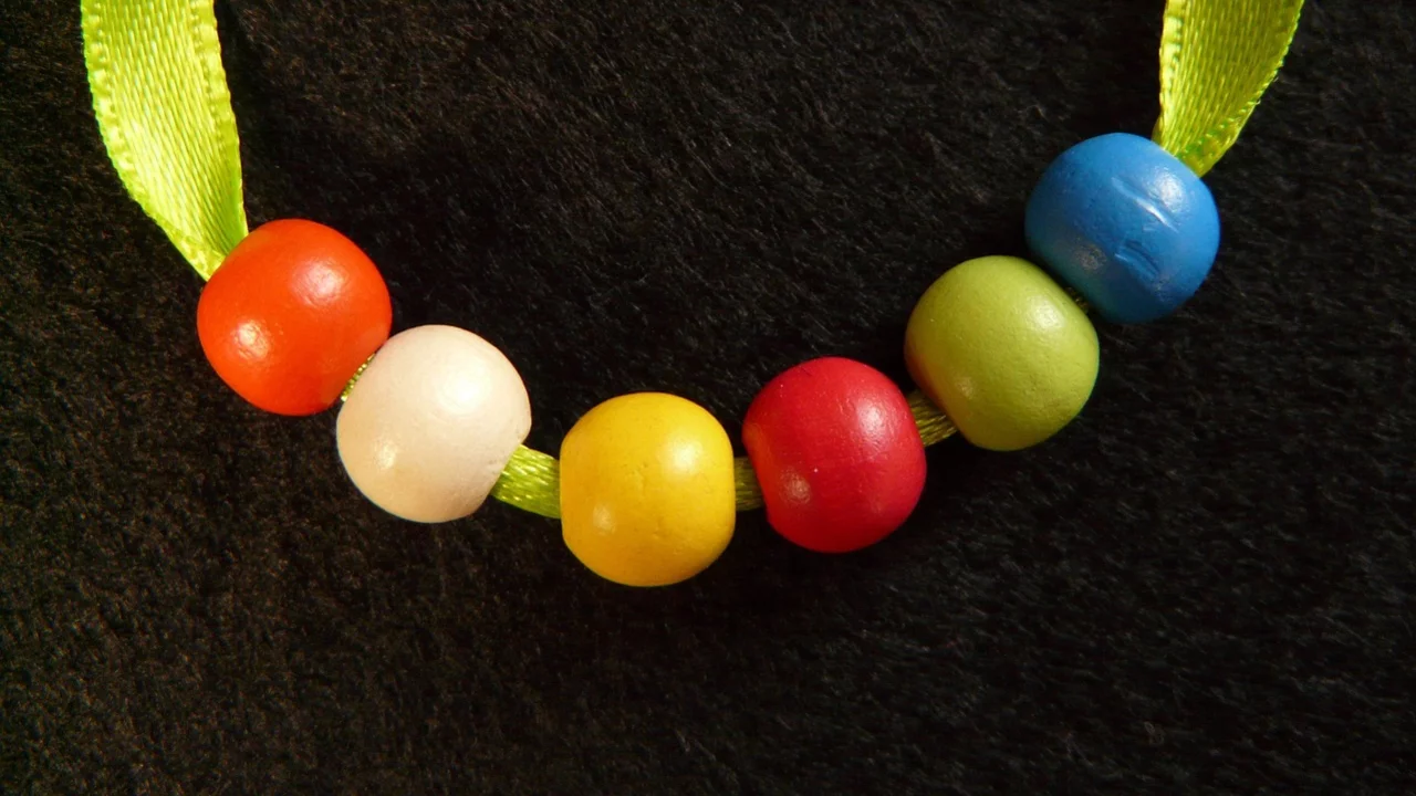 Eine farbenfrohe Kette aus sechs Holzperlen in Rot, Weiß, Gelb, Grün und Blau, auf einem zarten grünen Band. Die Perlen sind gleichmäßig angeordnet und verleihen der Kette ein fröhliches und handgefertigtes Aussehen.