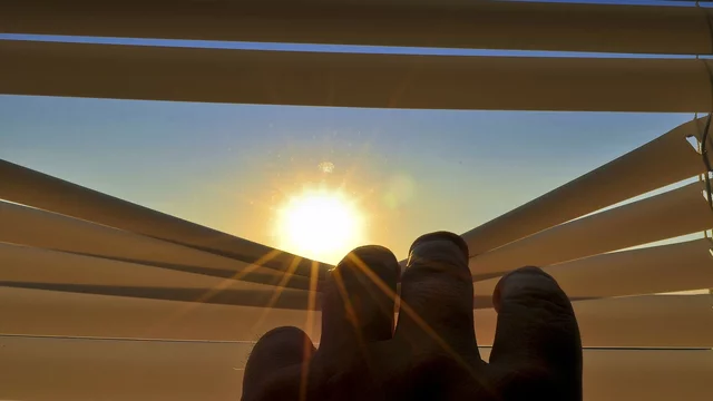 Blick durch eine Jalousie eines Fensters auf die Sonne