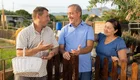 Gespräch unter Nachbarn am Gartenzaun. Zwei Männer und eine Frau unterhalten sich freundlich.