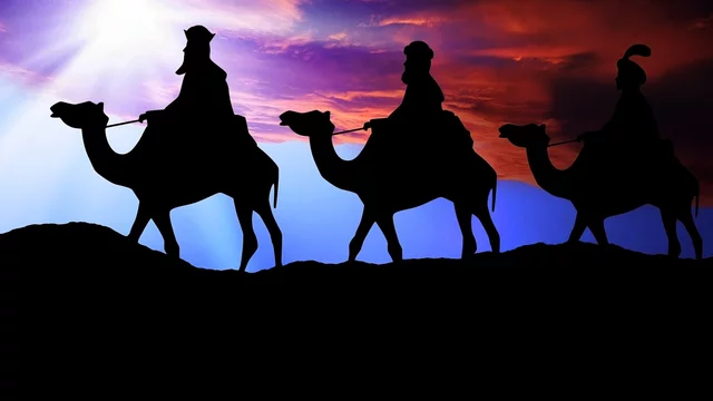 Drei Silhouetten von Kamelen mit Reitern sind vor einem farbenfrohen Sonnenuntergang dargestellt. Die Reiter tragen traditionelle Gewänder und bewegen sich in einer Reihe über eine Hügelkette. Das Bild vermittelt eine Atmosphäre von Reise und Entdeckung.