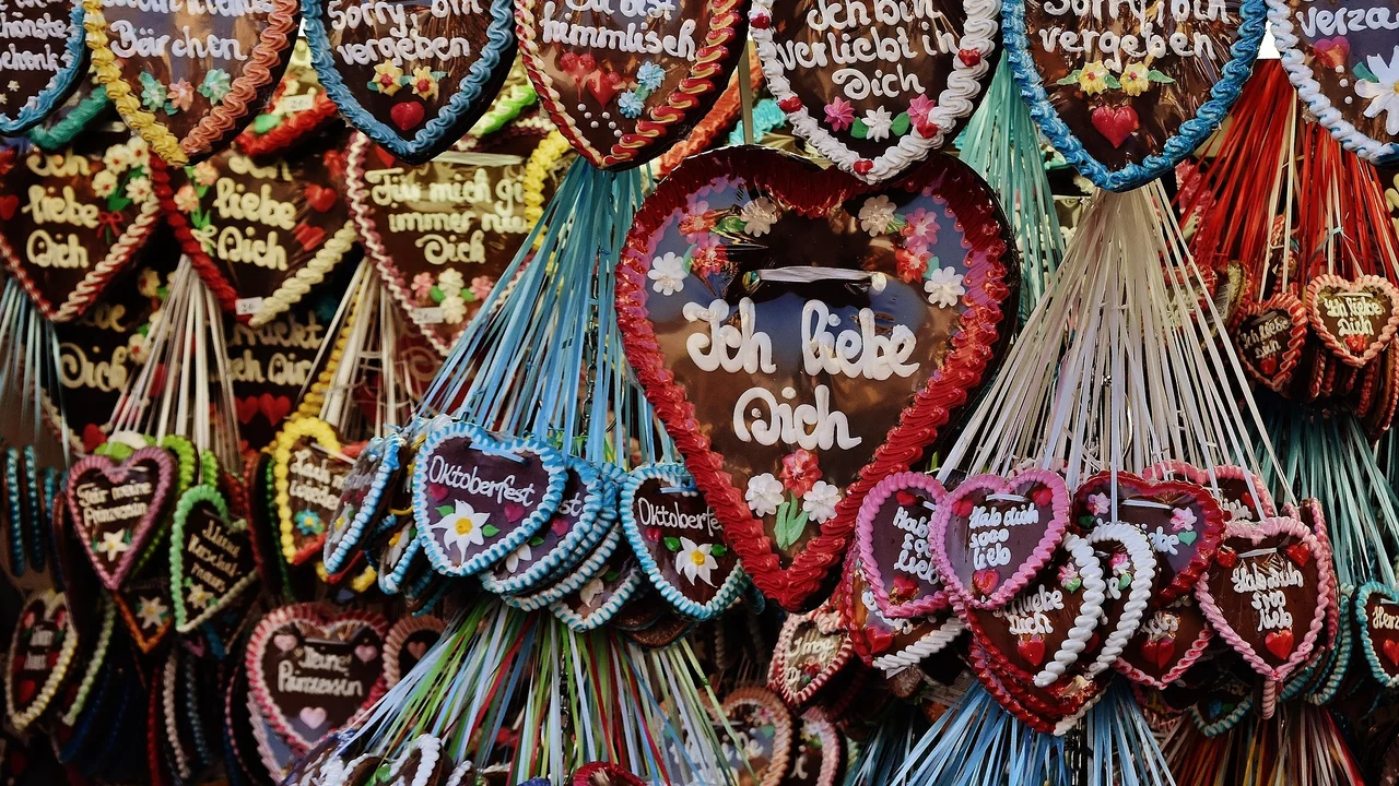 Eine bunte Wand mit Lebkuchenherzen, die verschiedene Botschaften tragen. Die zentralen Herzen zeigen die Aufschrift „Ich liebe Dich“ und „Ich bin verliebt in Dich“, umgeben von weiteren Herzen mit anderen Sprüchen wie „Sorry, bin vergeben“ und „Du hast mein Herz“.
