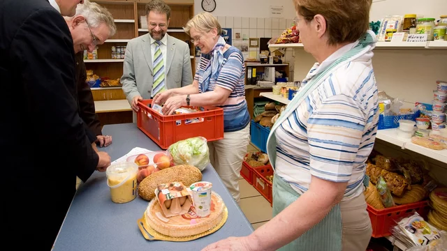 Mehrere Personen stehen an einem Tisch zusammen und bieten Essen an..