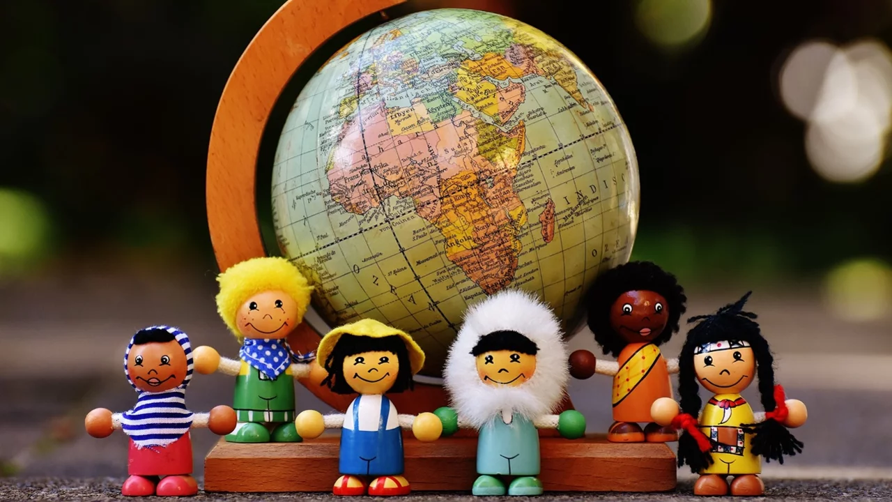 Eine bunte Gruppe von fünf Holzfiguren steht um einen Globus mit dem Kontinent Afrika. Die Figuren repräsentieren verschiedene Kulturen und Geschlechter, und der Globus symbolisiert die Vielfalt der Welt.