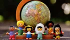 Eine bunte Gruppe von fünf Holzfiguren steht um einen Globus mit dem Kontinent Afrika. Die Figuren repräsentieren verschiedene Kulturen und Geschlechter, und der Globus symbolisiert die Vielfalt der Welt.