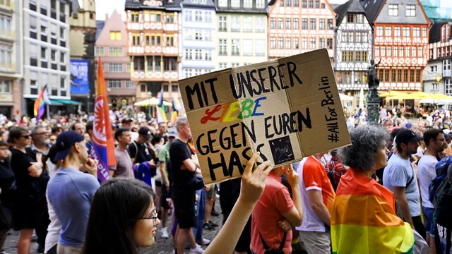Eine Person hält ein Schild mit der Aufschrift "Mit unserer Liebe gegen euren Hass" hoch. Im Hintergrund versammeln sich zahlreiche Menschen zur Unterstützung von LGBT-Rechten. Gemeinsam zeigen sie Haltung und Solidarität.