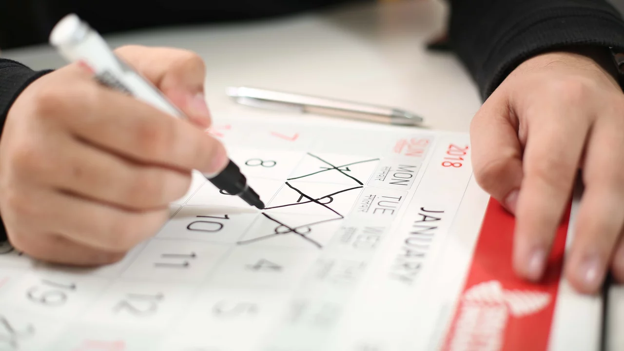 Eine Hand hält einen schwarzen Marker und kreuzt mehrere Tage auf einem Monatskalender für Januar 2018 an. Der Kalender zeigt die Wochentage und die Nummern der Tage an.