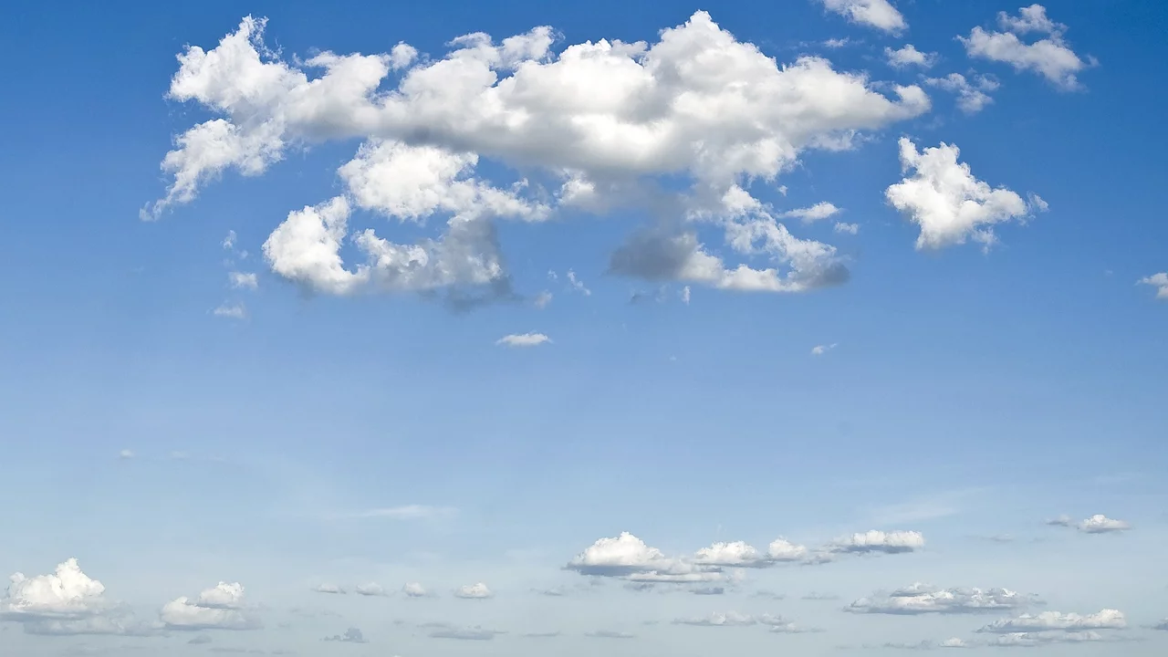 Ein klarer blauer Himmel mit mehreren weißen Wolken, die sich in unterschiedlichen Formen und Größen verteilen. Die Wolken sind weich und flauschig, der Gesamteindruck ist friedlich und einladend.