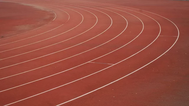 Ein Sportplatz mit einem rotenlaufband. Die weißen Bahnen sind in geschwungener Form angeordnet.
