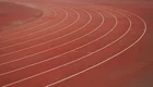 Ein Sportplatz mit einem rotenlaufband. Die weißen Bahnen sind in geschwungener Form angeordnet.