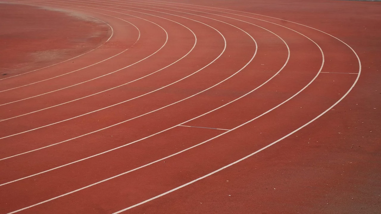Ein Sportplatz mit einem rotenlaufband. Die weißen Bahnen sind in geschwungener Form angeordnet.