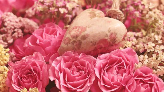Ein Bouquet aus pechschwarzen Rosen in verschiedenen Rosa- und Pinktönen, umgeben von zarten, hellen Blumen. In der Mitte liegt ein Herz aus Holz mit floralen Mustern, das die romantische Stimmung unterstreicht.