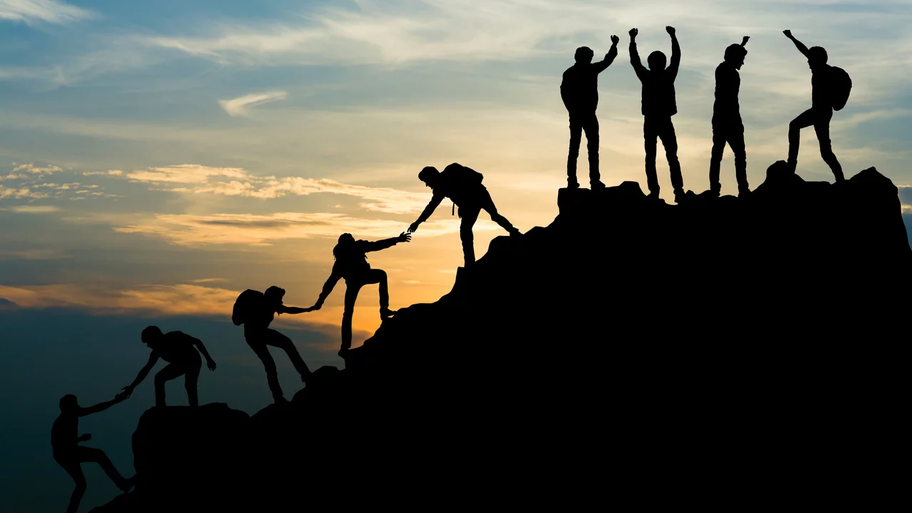 Menschen besteigen bei Sonnenaufgang einen steilen Berggipfel. Sie bilden eine Kette. Die noch am Aufstieg sind helfen ich gegenseitig, indem sie sich die Hände reichen. Vier Leute stehen schon auf dem Gipfel und haben die Arme zum Jubel erhoben.